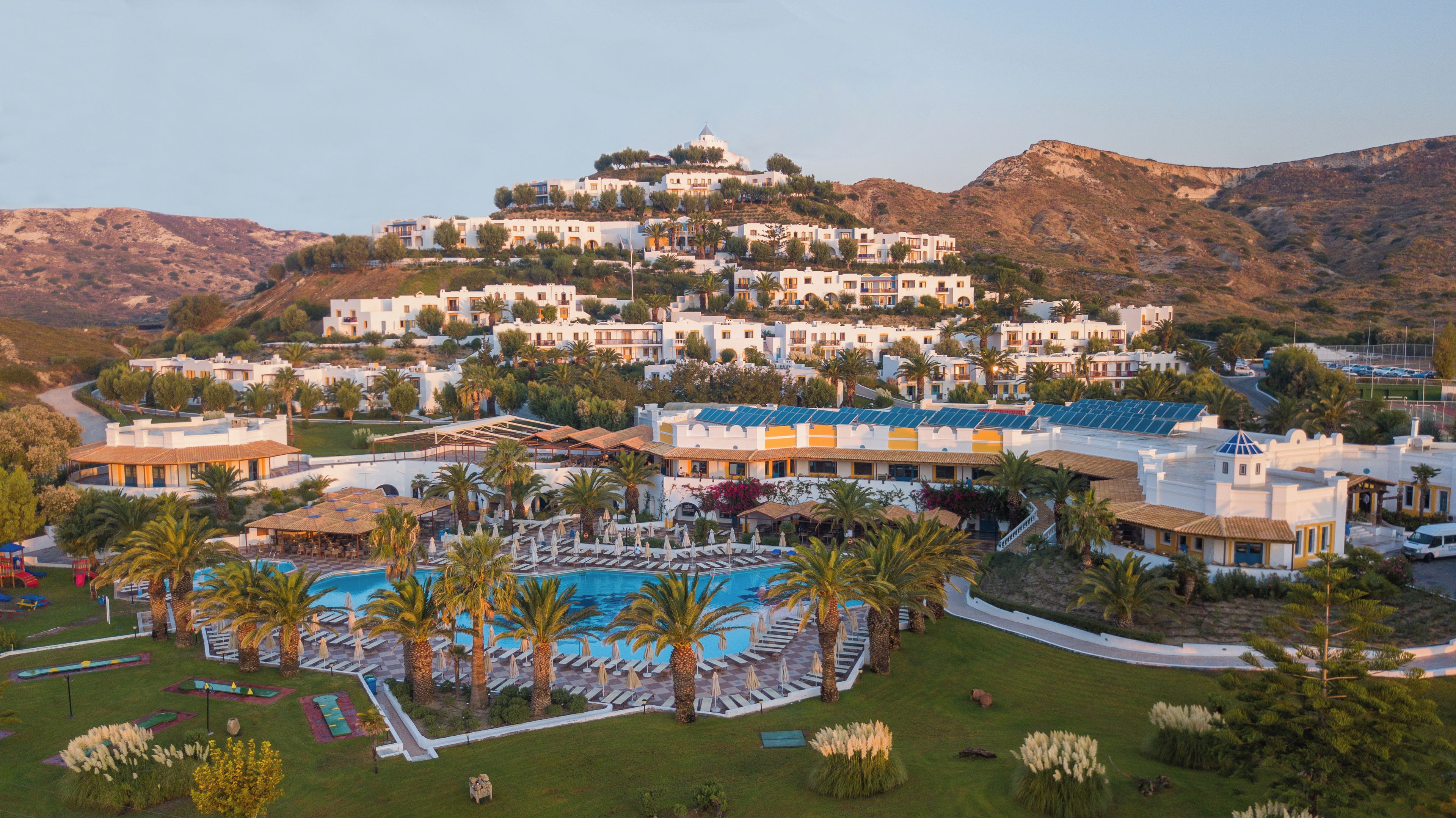 A resort with a swimming pool, sun loungers, and a view of the surrounding hills.