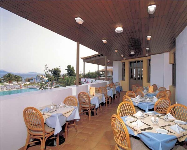An outdoor dining area with tables set for two, overlooking a pool and a scenic view.
