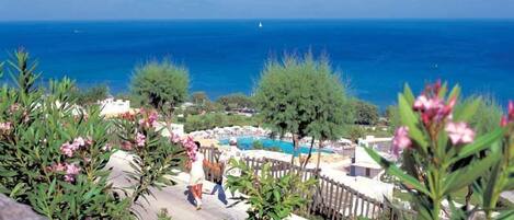 A resort with a pool, a view of the sea, and a person walking.