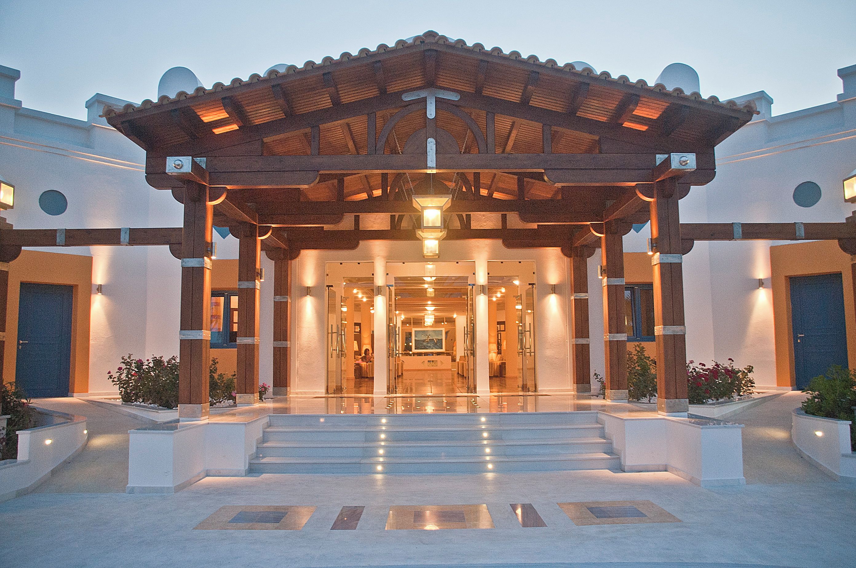 A hotel entrance with a covered walkway, steps leading up to the entrance, and a reception area visible through the glass doors.