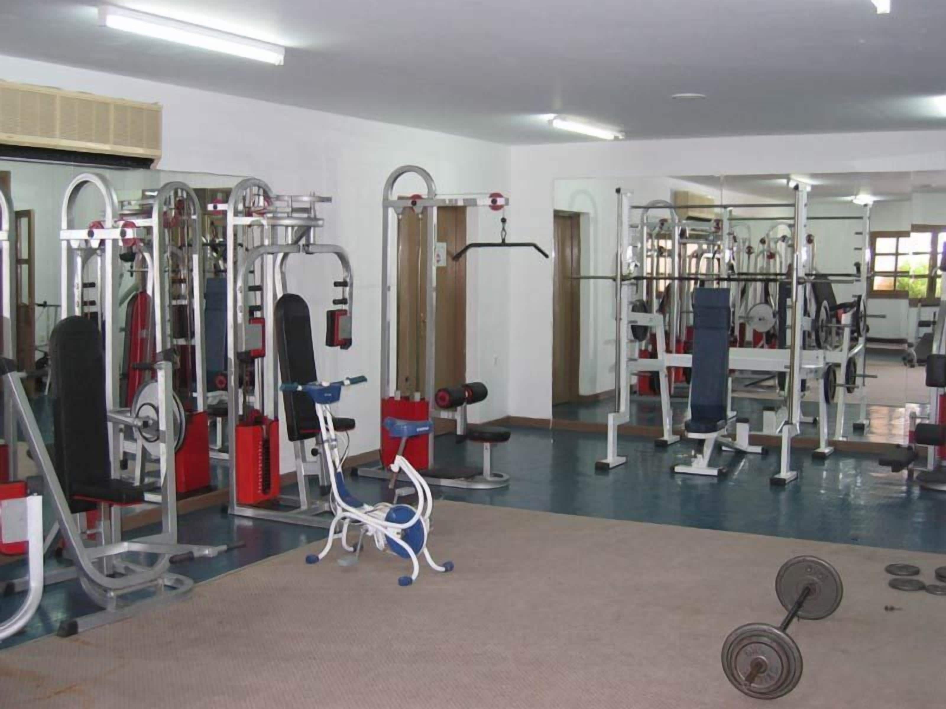 A gym with various exercise machines, mirrors, and a weight rack.
