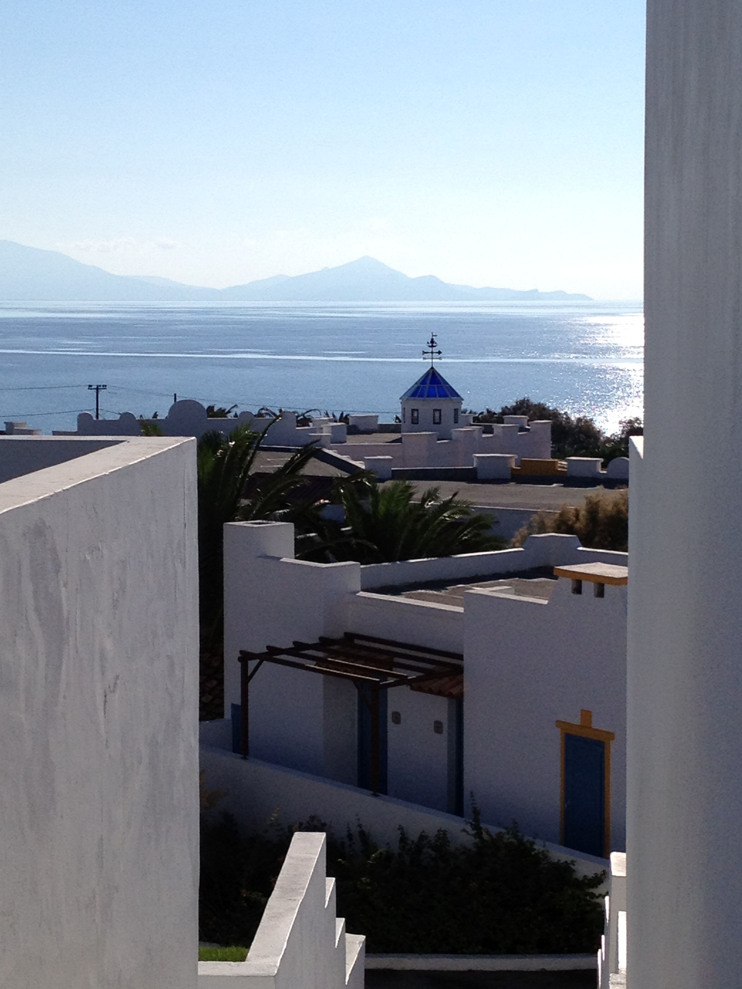 A coastal view with a building featuring a blue-domed structure, white walls, and a clear view of the sea and distant mountains.