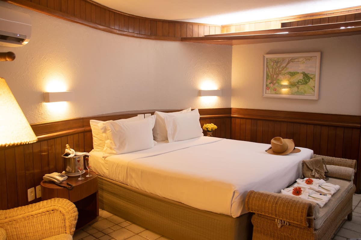 A neatly arranged hotel room with a large bed, a bedside table with a lamp, a telephone, and a wicker chair.