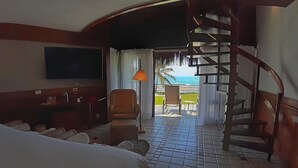 A hotel room with a bed, a desk, a chair, a TV, a staircase, and a view of the ocean.