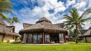 A resort with thatched-roof villas, a pool area with lounge chairs, and palm trees.