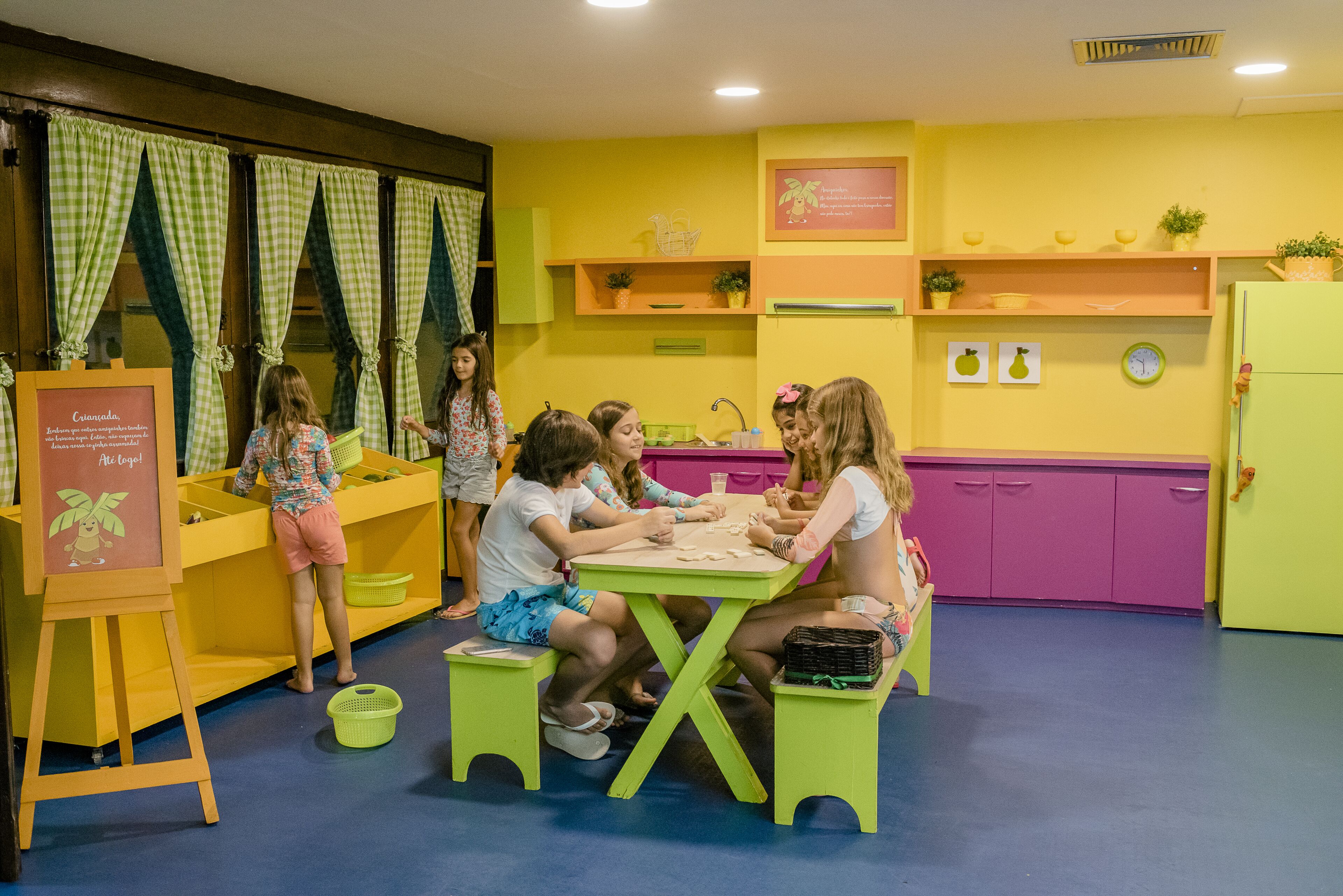 A group of children engaged in a craft activity in a brightly colored room with a play kitchen area.