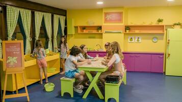 A group of children engaged in a craft activity in a brightly colored room with a play kitchen area.
