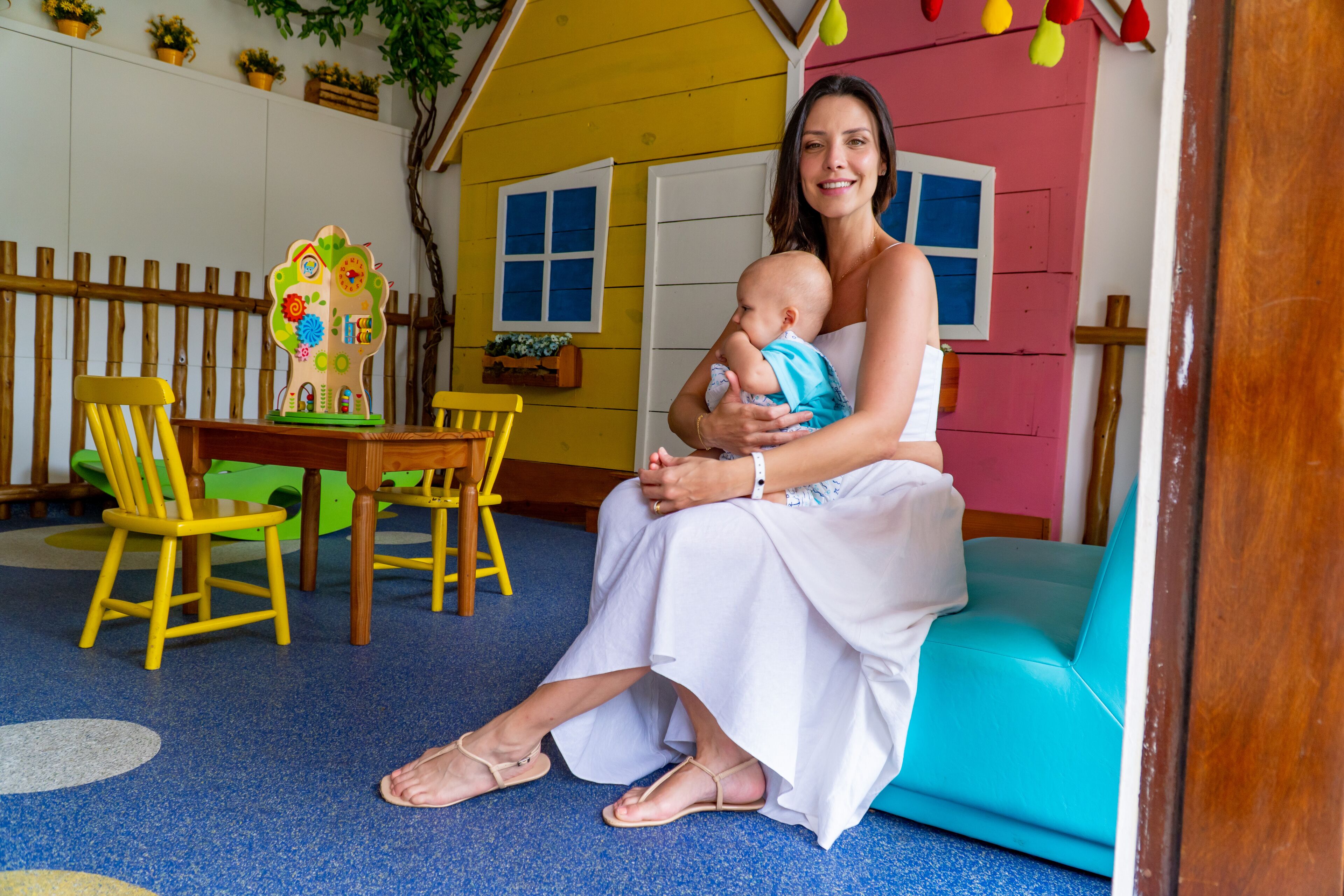 A woman sitting on a blue couch in a room with a wooden fence, a wooden table, and a colorful playhouse in the background.