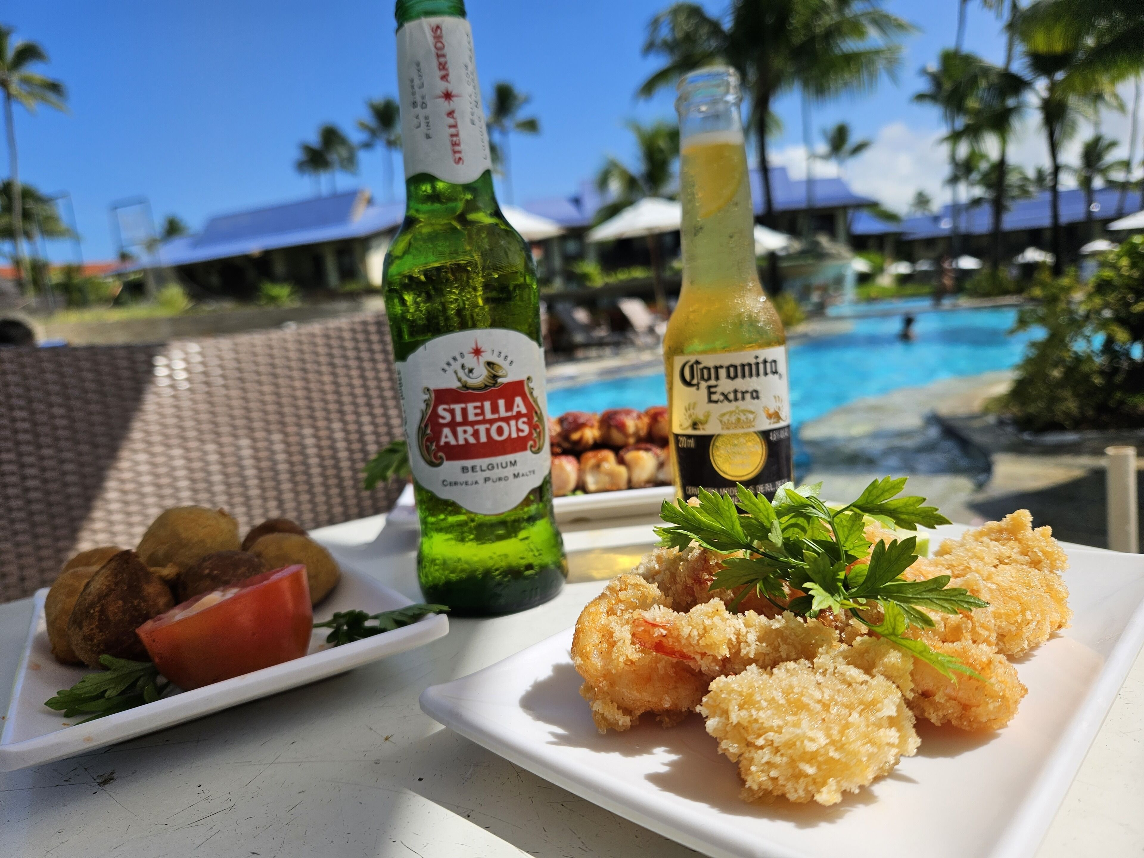 A table with a bottle of Stella Artois, a bottle of Corona Extra, and a plate of food including breaded shrimp and vegetables.