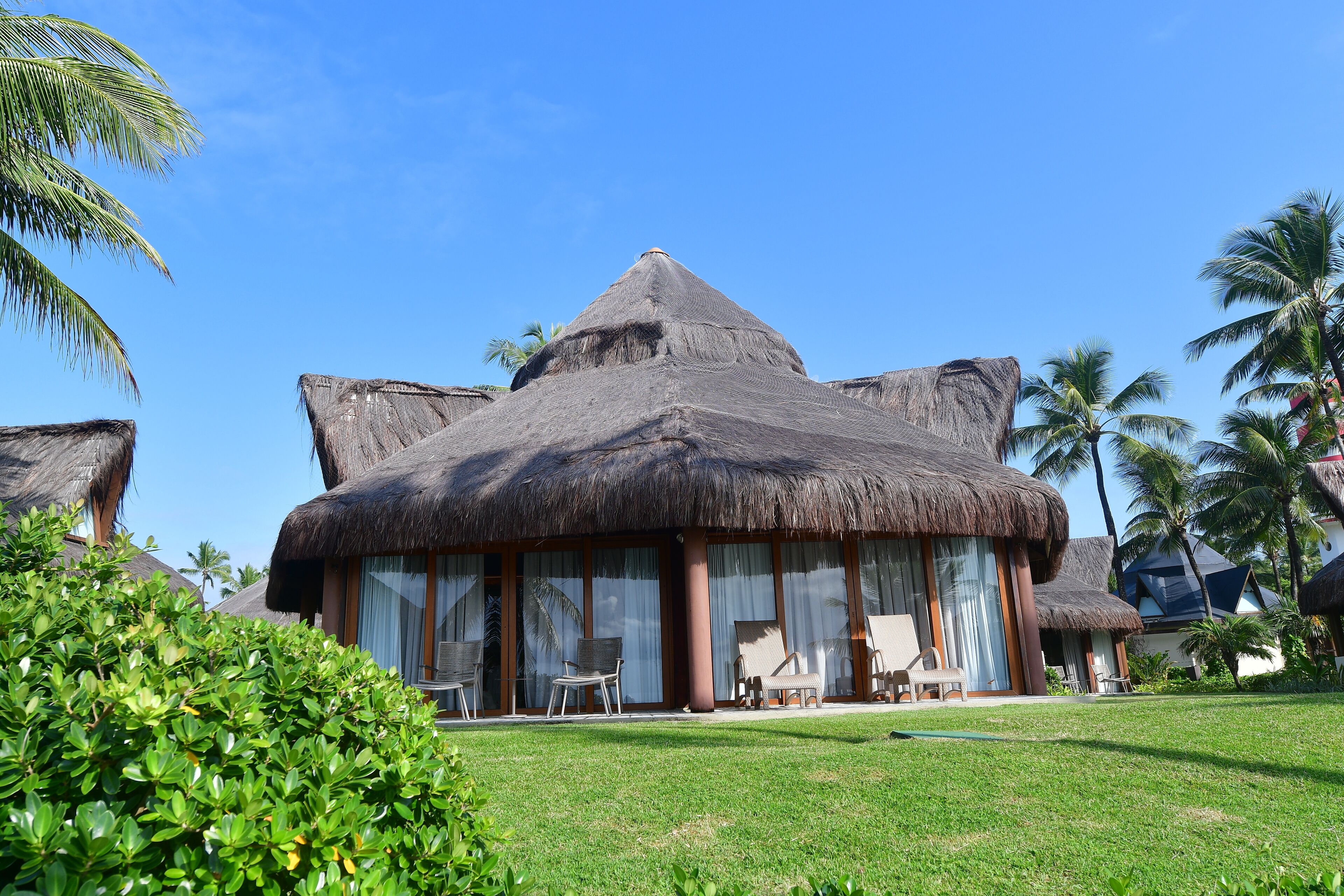 Ein Resort mit strohgedeckten Gebäuden, großen Fenstern und einem gepflegten Rasen.