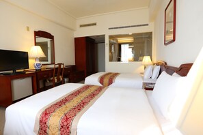 A hotel room with two beds, a desk with a television, a chair, and a mirror.