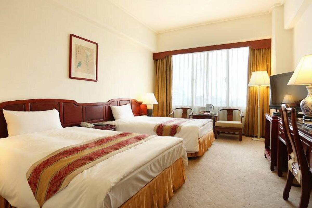 A hotel room with two beds, a desk, a chair, a television, and a window with curtains.