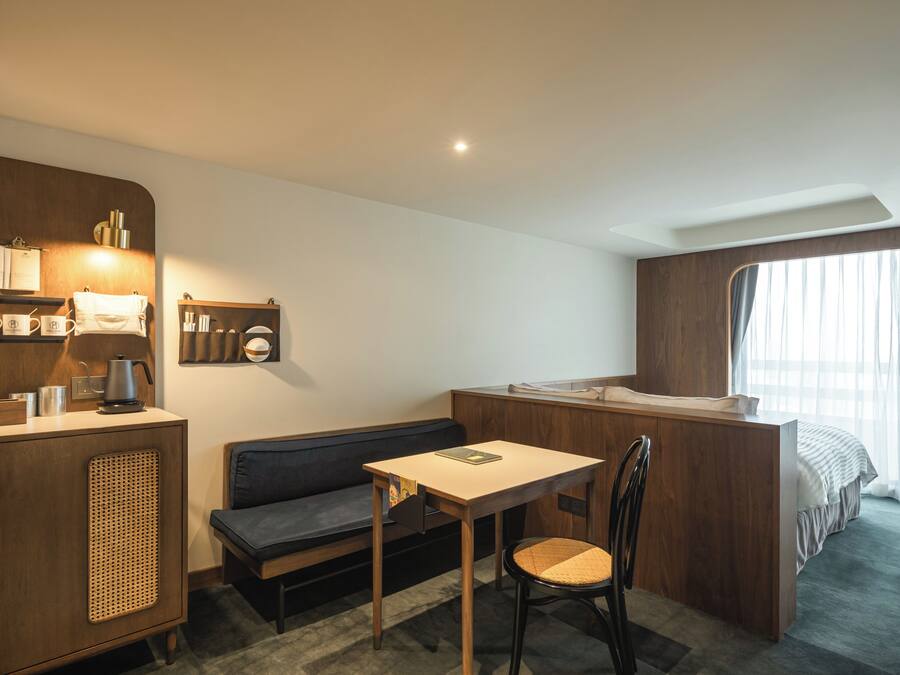 A compact hotel room with a kitchenette, a sofa, a small table, and a single bed.