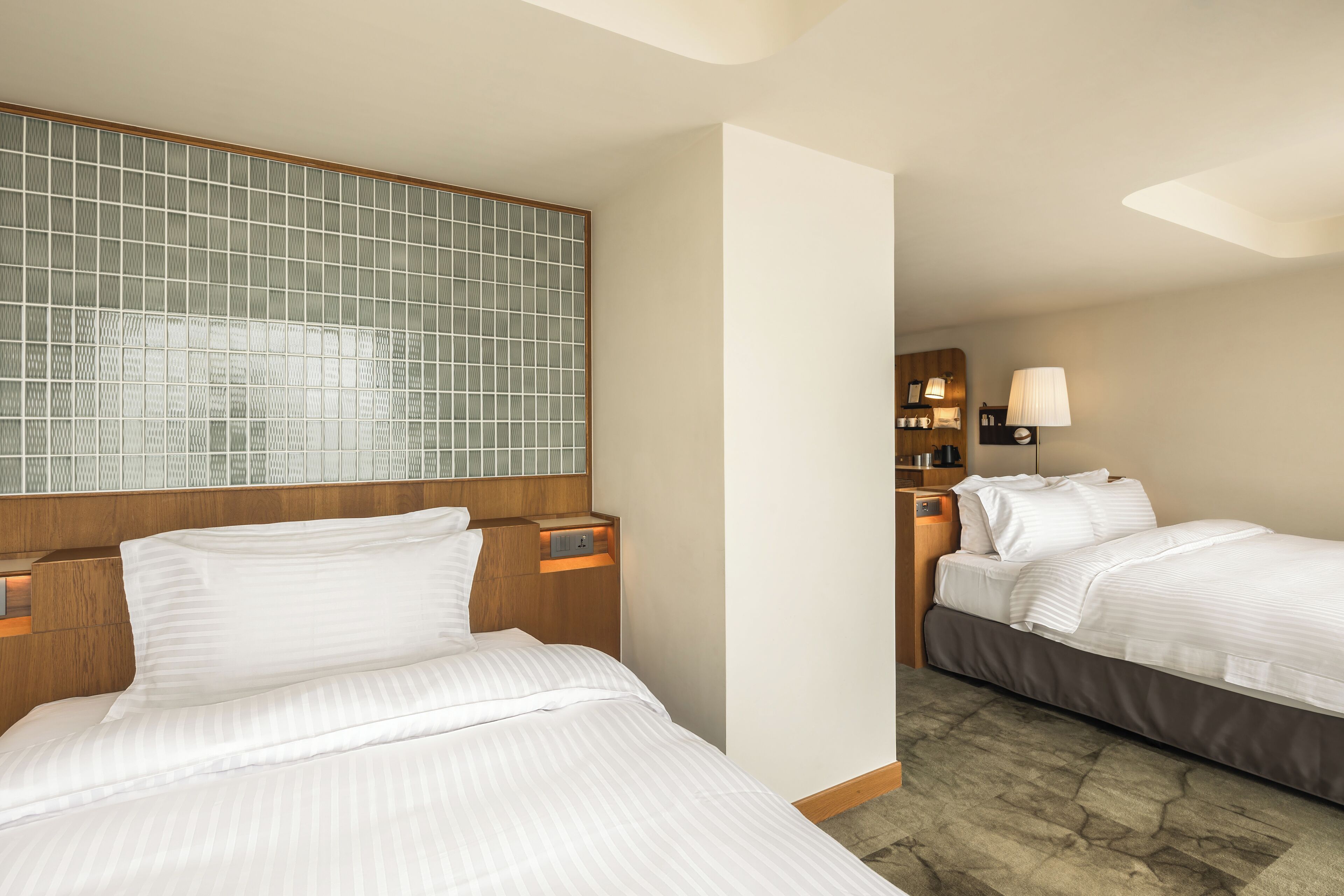 A hotel room with two beds, a large window with a view, a wooden headboard, and a nightstand with a lamp.