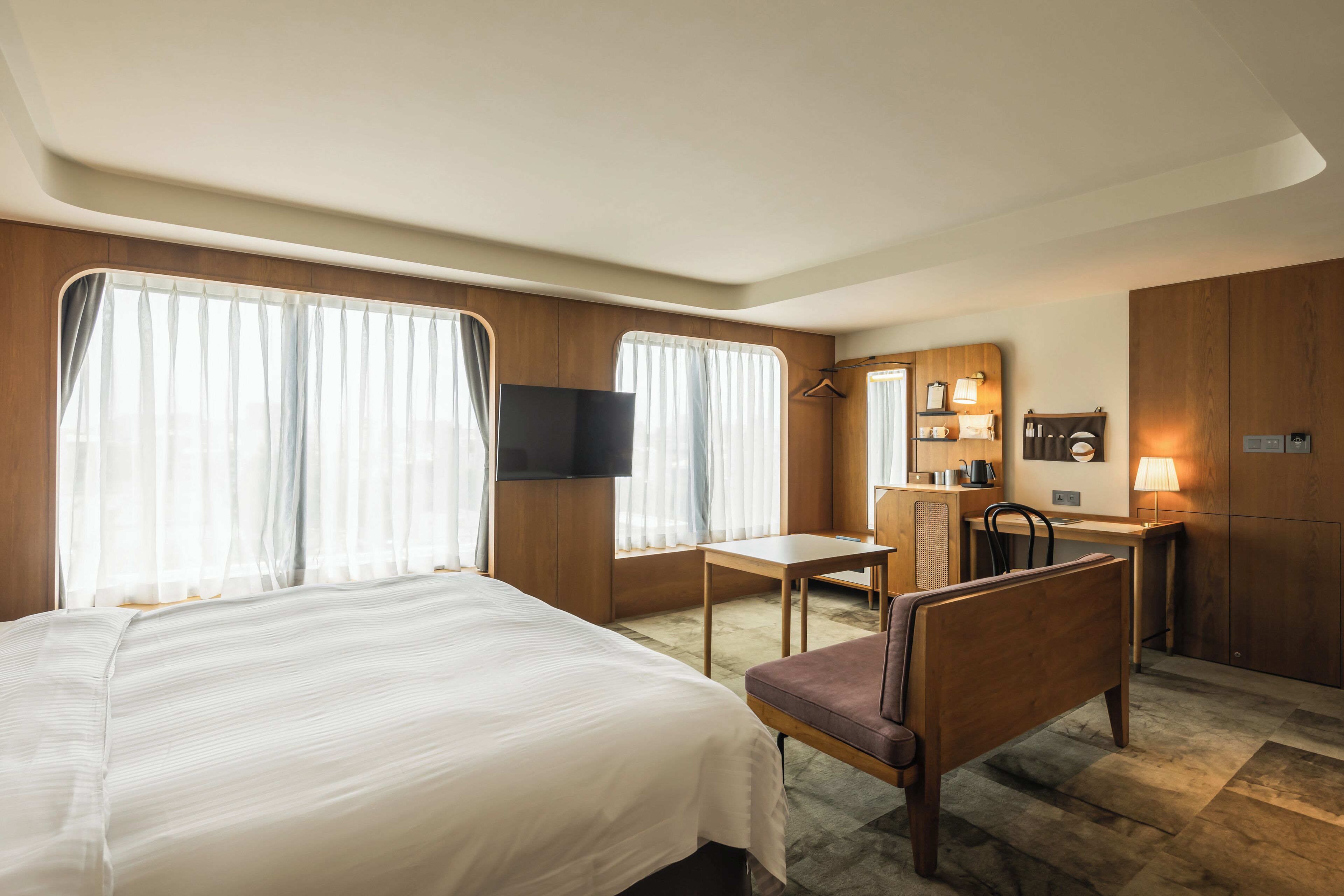 A hotel room with a bed, a desk, a chair, a TV, and a wardrobe.