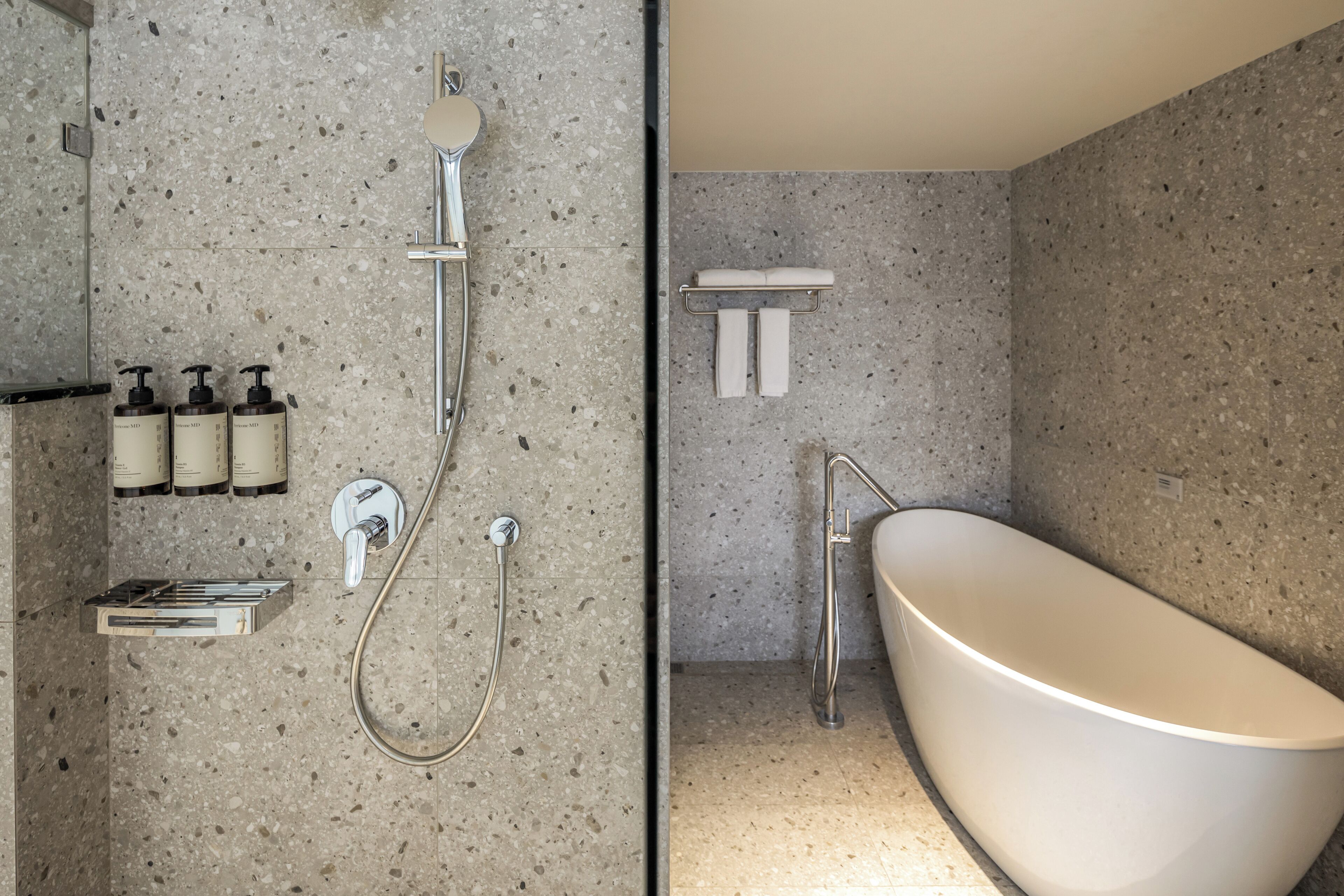 A modern bathroom with a freestanding bathtub, a shower with a handheld showerhead, and a wall-mounted soap dispenser.