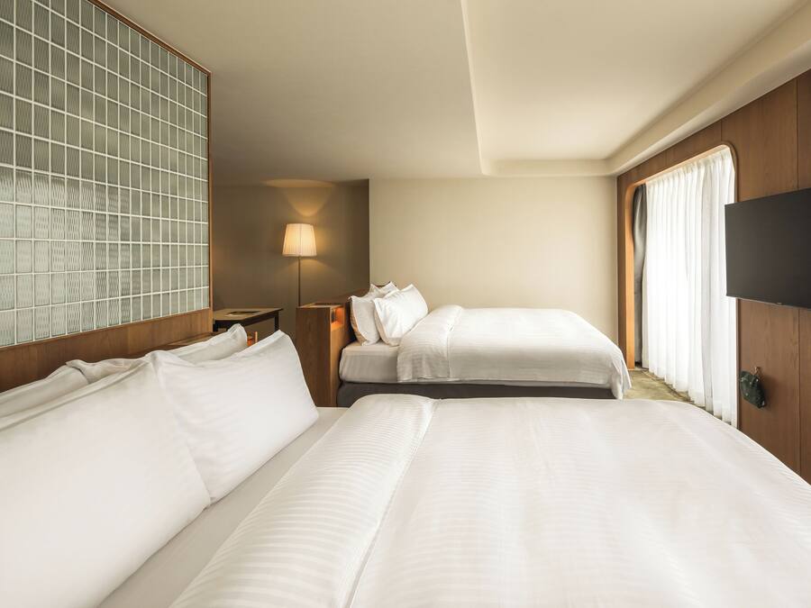 A hotel room with two beds, a TV, a lamp, and a window with curtains.