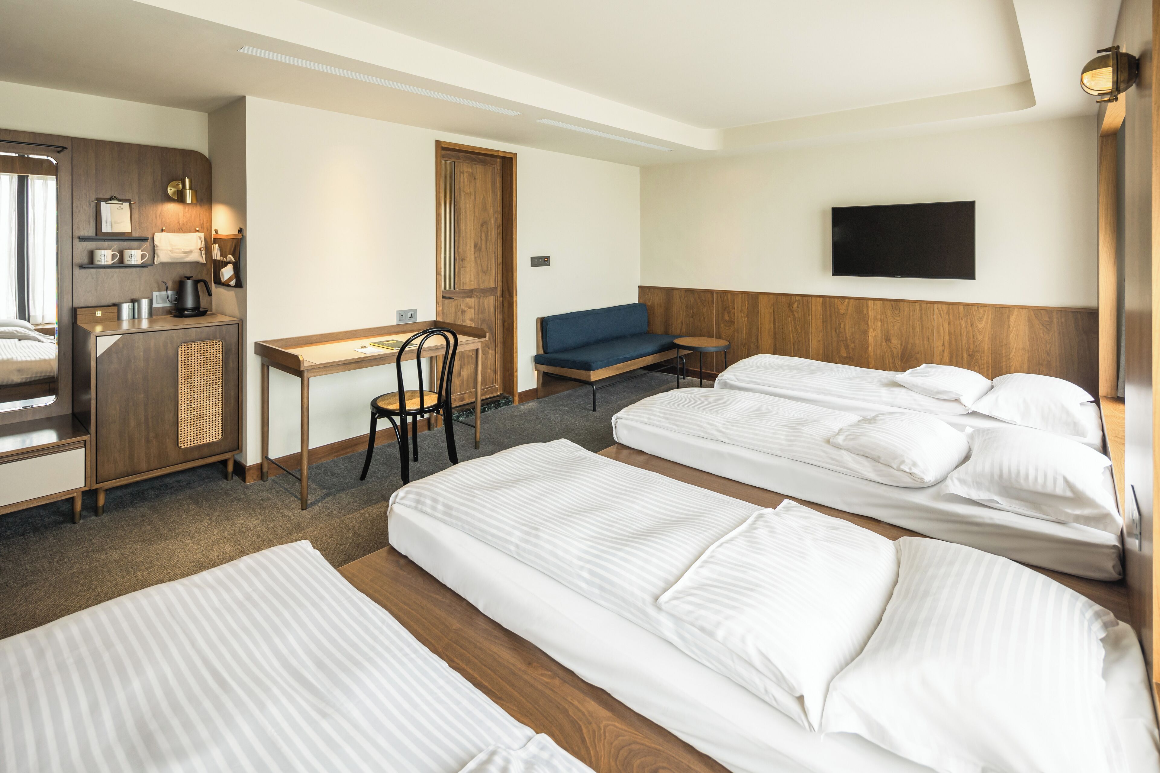 A hotel room with two beds, a desk, a chair, a sofa, a TV, and a coffee machine.