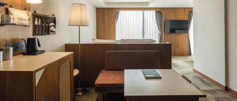 Una habitación de hotel pequeña con cama, escritorio, silla, mesa, lámpara, televisor y ventana con cortinas.