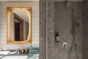 A bathroom with a large mirror, a shower, and a sink with toiletries. - Provintia Hotel (Tainan)