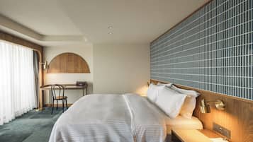 A hotel room with a bed, desk, chair, and a large window with curtains.