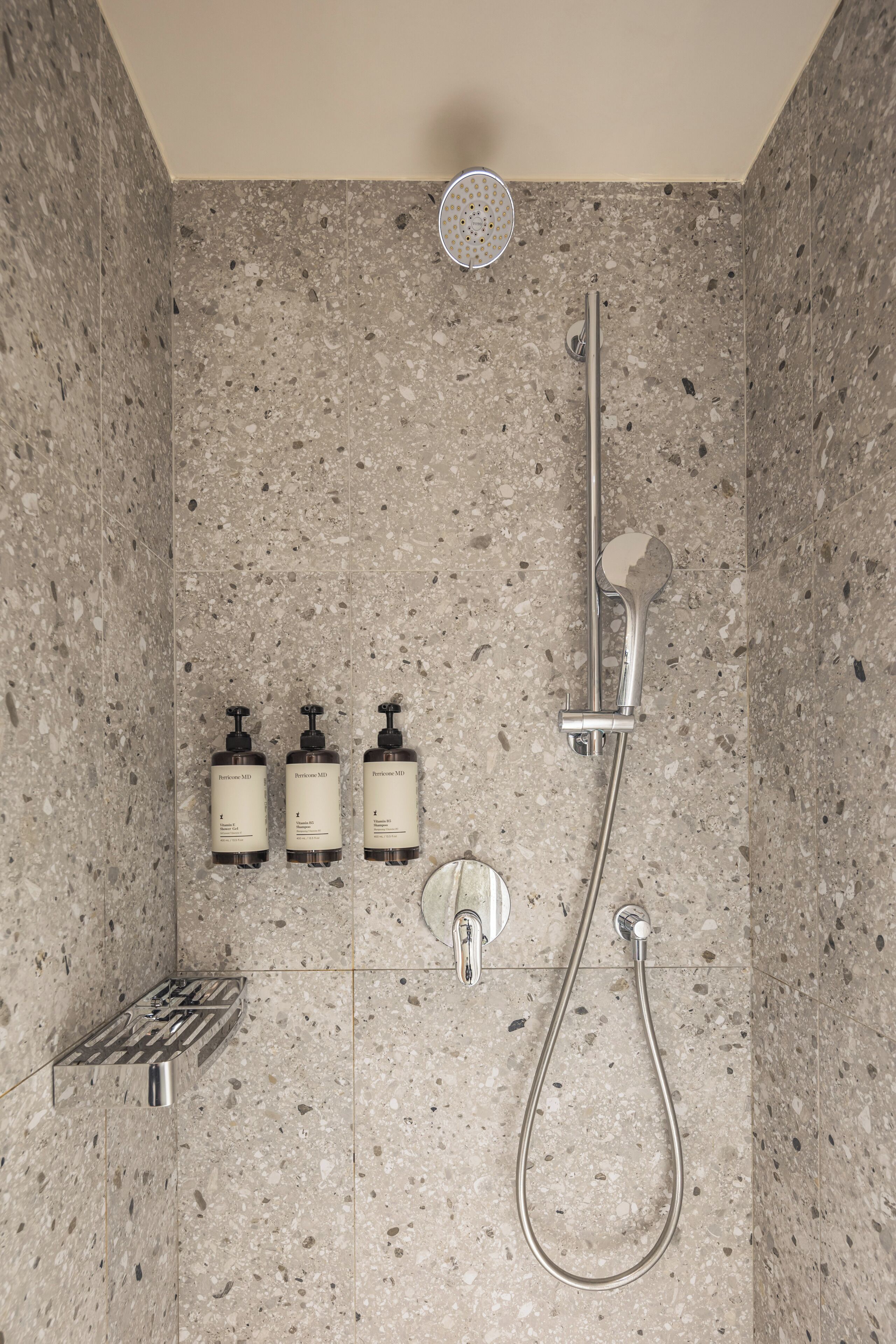 A shower with a handheld showerhead, a wall-mounted faucet, and three bottles of shampoo.
