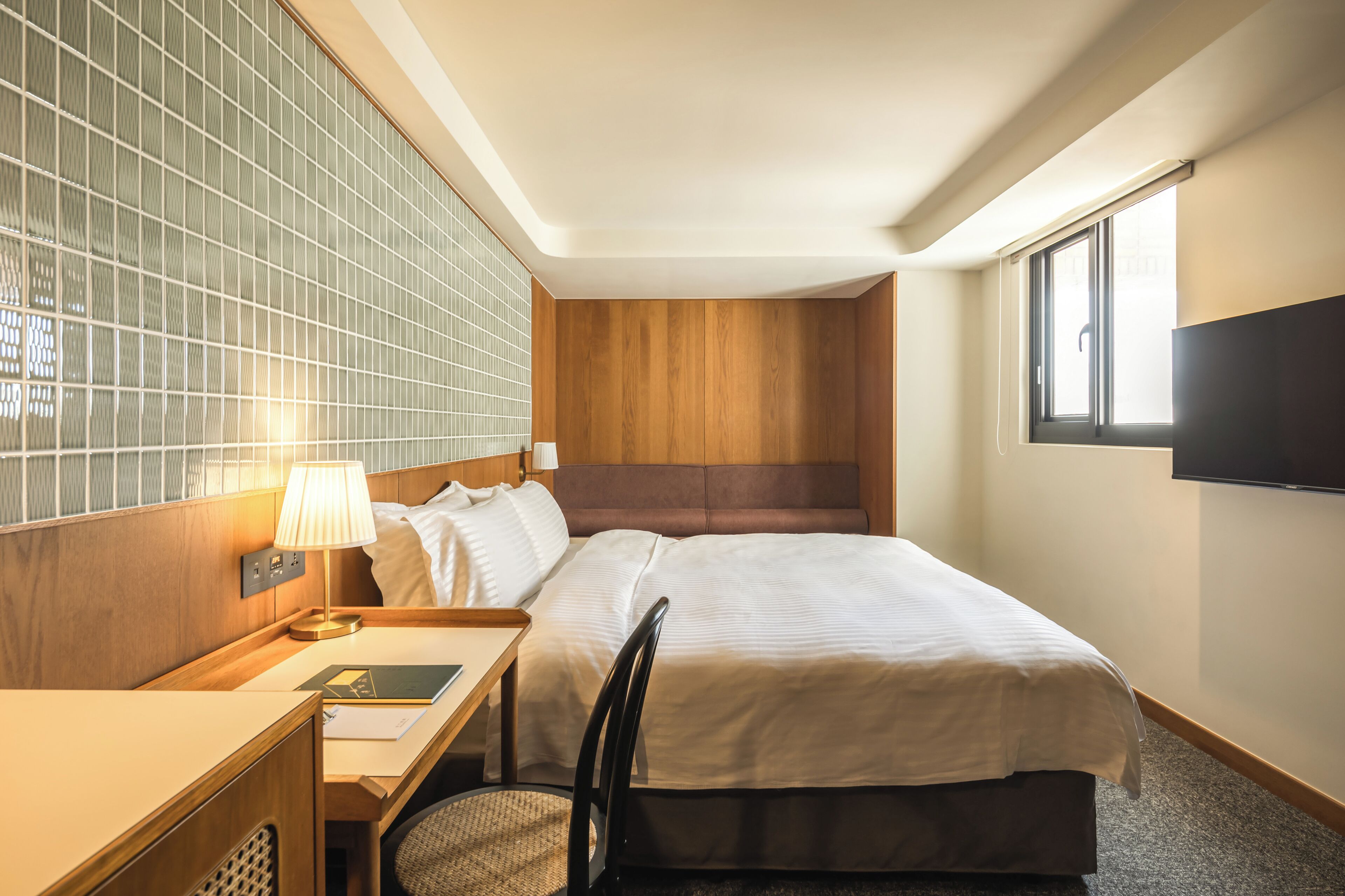 Habitación de hotel con una cama grande, un escritorio con lámpara, una silla y un televisor montado en la pared.