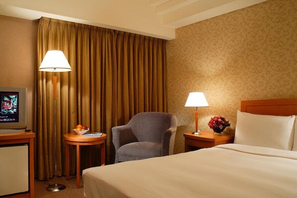A hotel room with a bed, a chair, a TV, two lamps, and a small table with a fruit bowl. - San Want Hotel Taipei (Taipei)