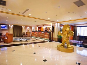 A hotel lobby with a reception desk, seating area, and a large golden statue.