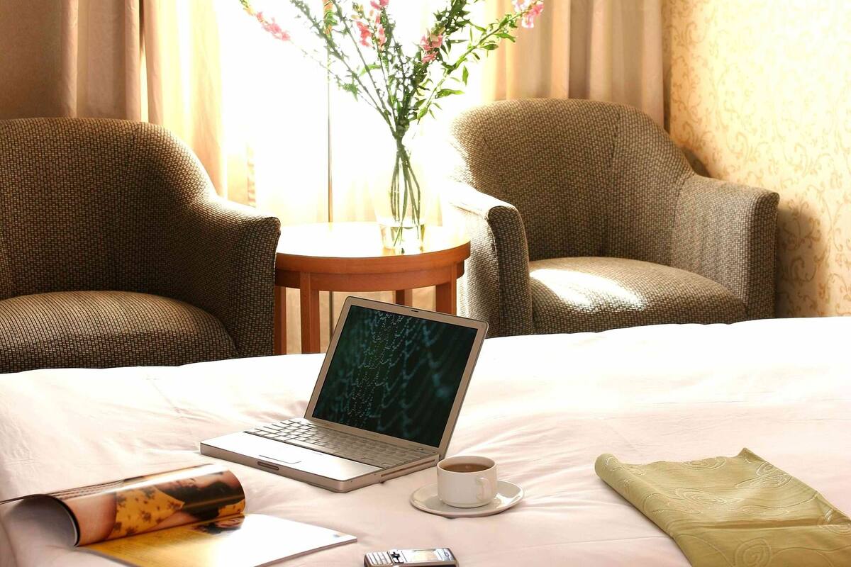 Habitación de hotel con una cama, una computadora portátil, una taza de café, un control remoto y un jarrón con flores.