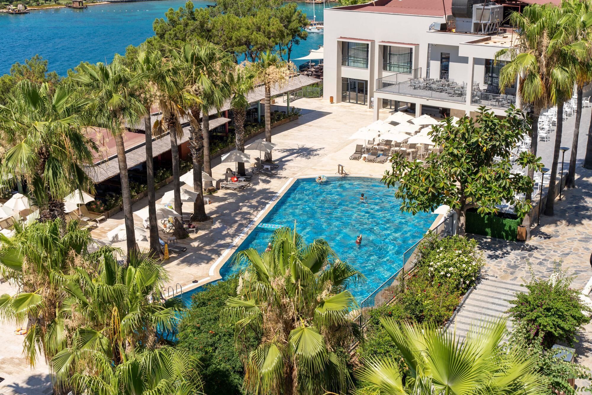 Un complexe hôtelier doté d’une piscine entourée de palmiers et de chaises longues.
