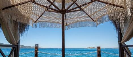 A wooden deck with a thatched umbrella, wooden lounge chairs, and mattresses.