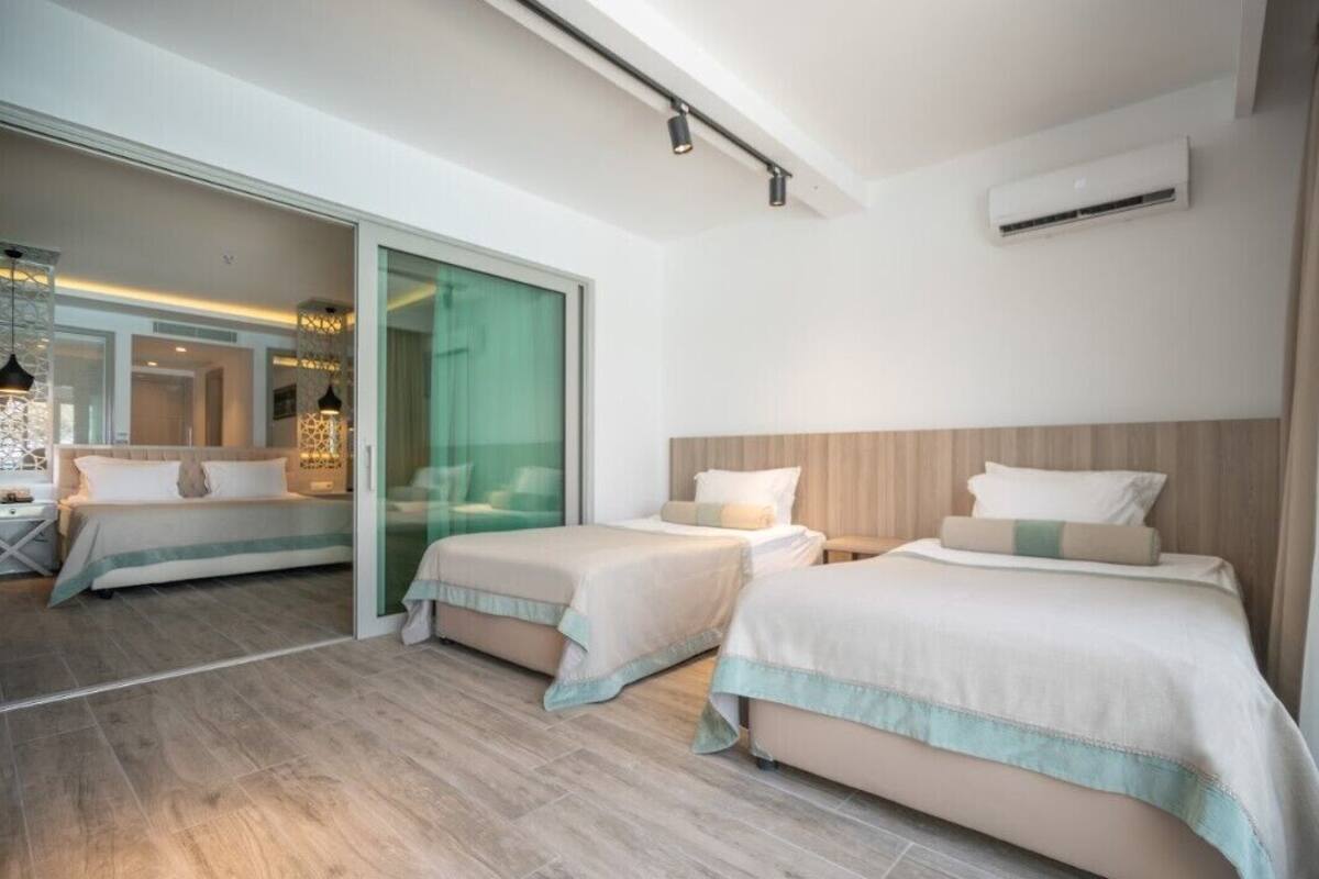 Une chambre d’hôtel moderne avec deux lits, une porte-fenêtre coulissante donnant sur un balcon et une salle de bain visible.