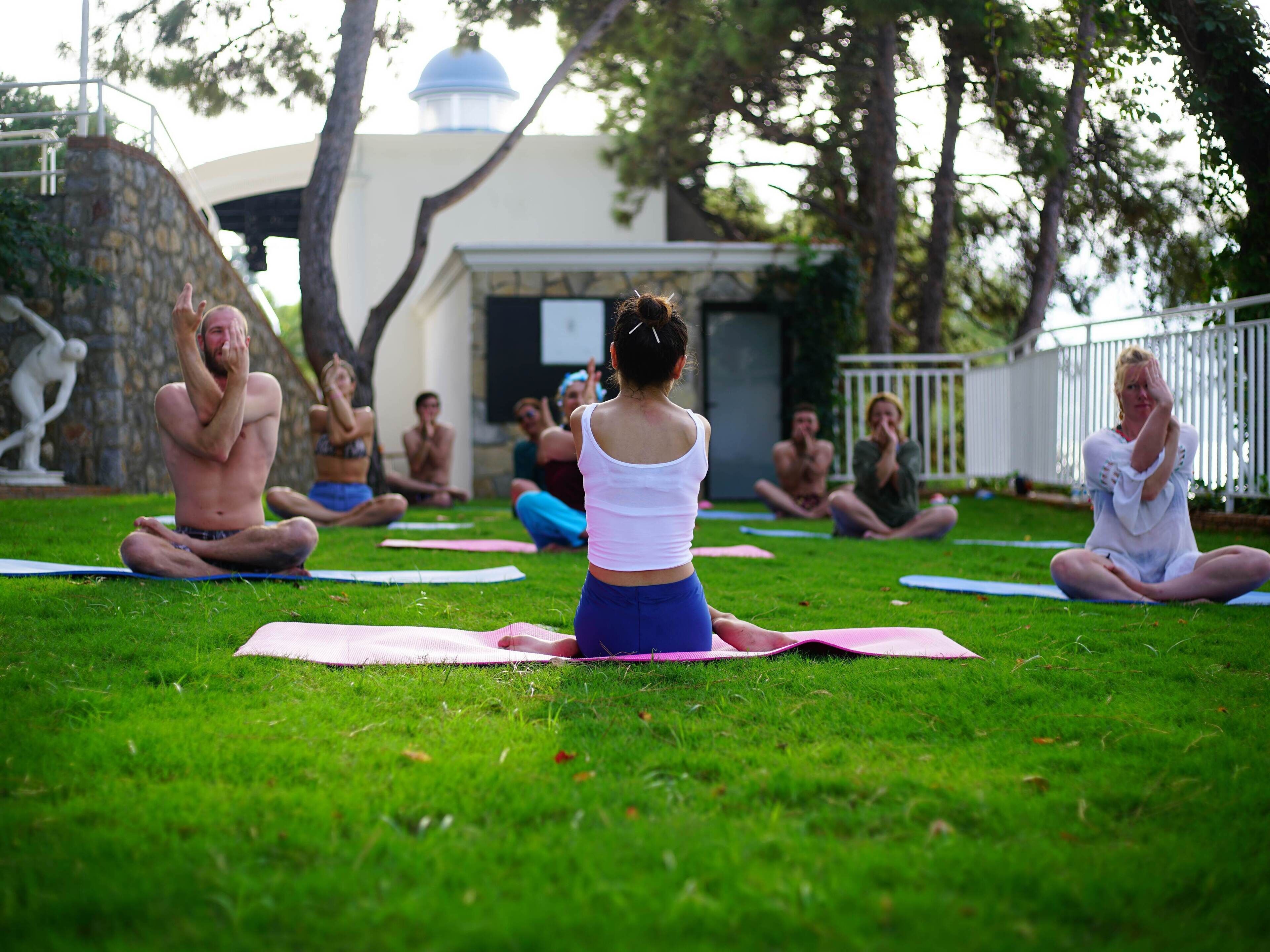 A group of people practicing yoga on grass mats outdoors.