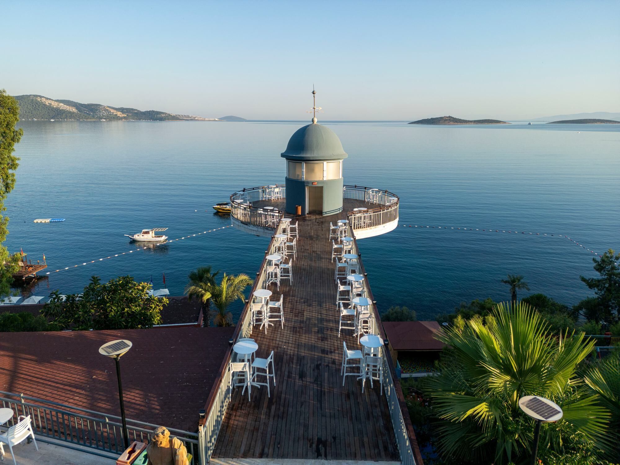 A deck with outdoor seating overlooking a calm sea, a central dome structure, and a distant shoreline.