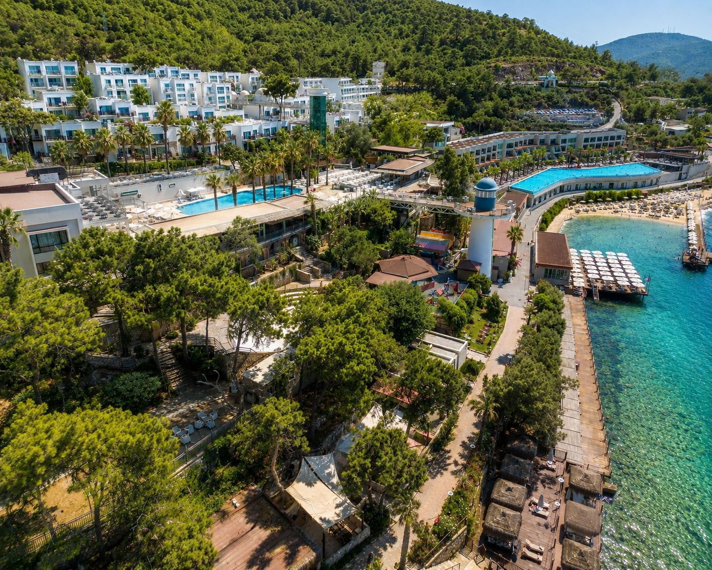 A coastal resort with multiple buildings, a swimming pool, and a pier extending into the sea.