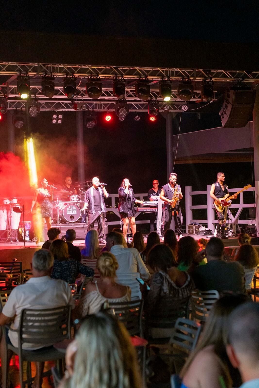 A band performing on a stage with a crowd seated in front.