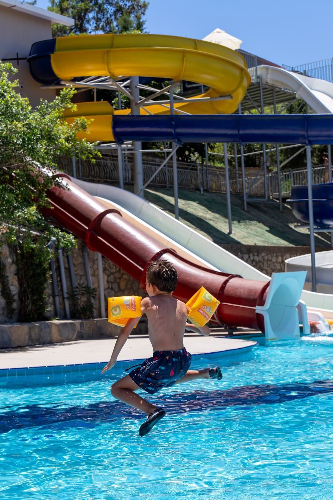 A child in a swimming pool with water slides in the background.