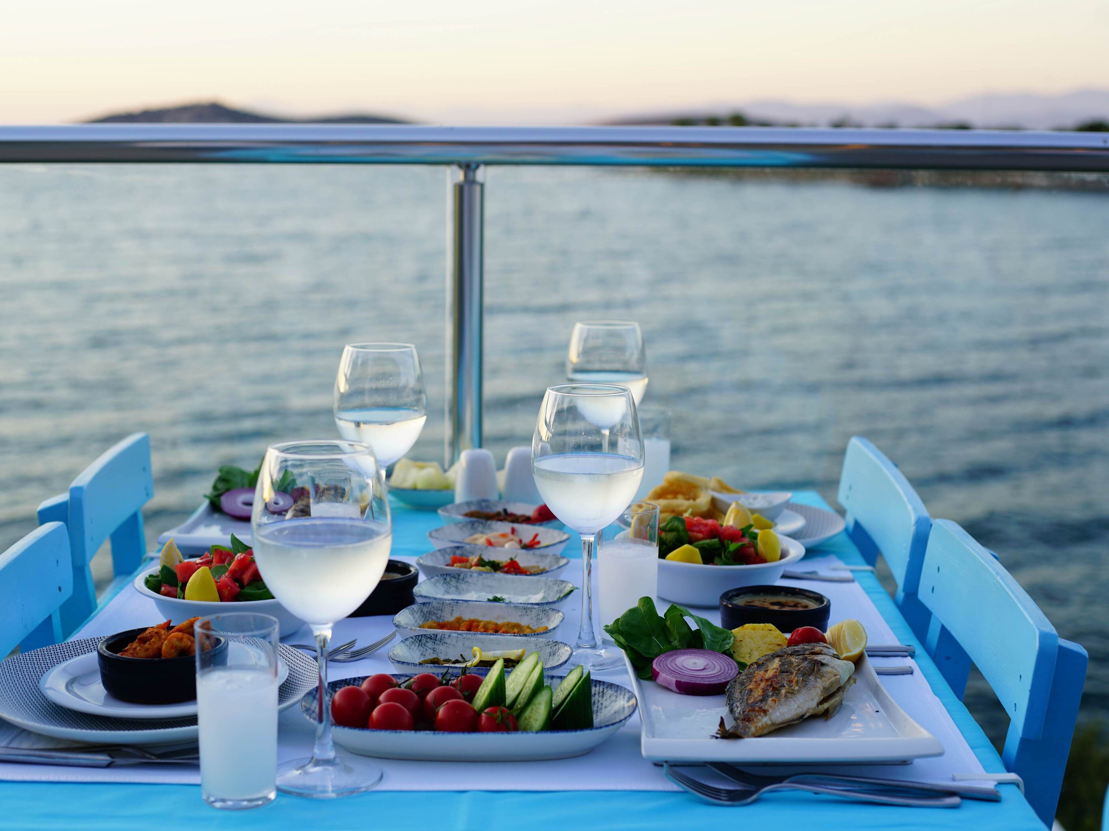 A table set with various dishes and drinks, overlooking a body of water.