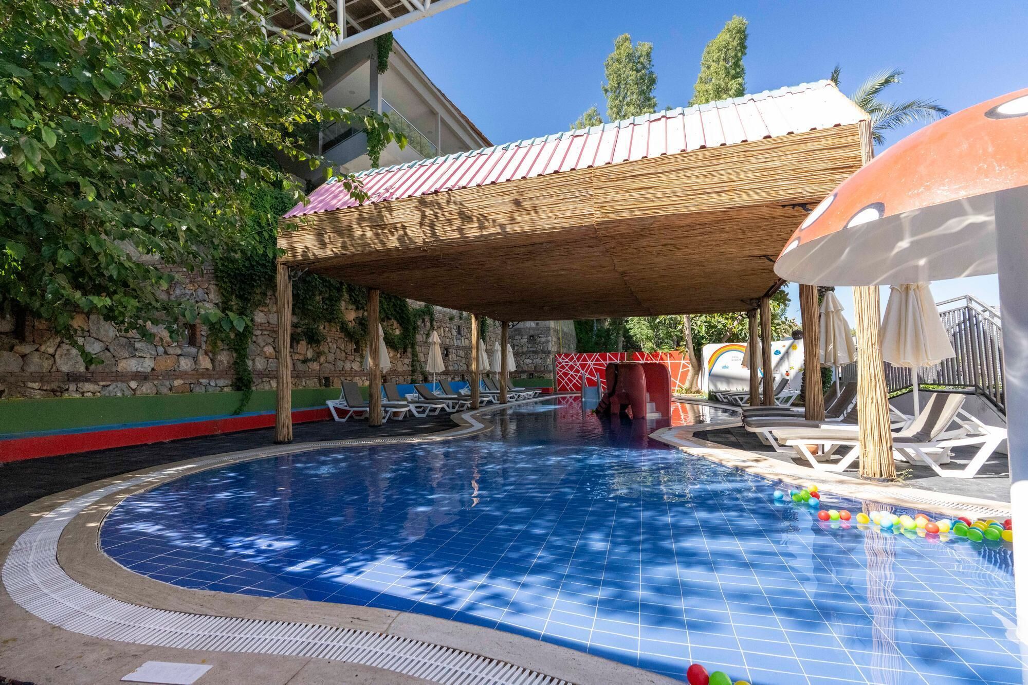 A swimming pool with lounge chairs and umbrellas, surrounded by stone walls and greenery.