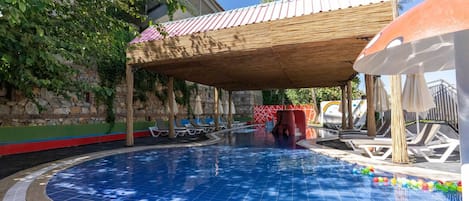 Una piscina con sillas de descanso y sombrillas, rodeada de muros de piedra y vegetación.