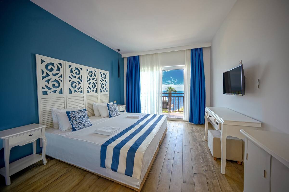 Une chambre d’hôtel avec un grand lit, un bureau, une télévision et un balcon donnant sur la mer.