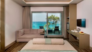 A hotel room with a bed, a sofa, a dining table with chairs, a TV, and a view of the sea. - Blue Dreams Resort-Ultra All Inclusive (Bodrum)