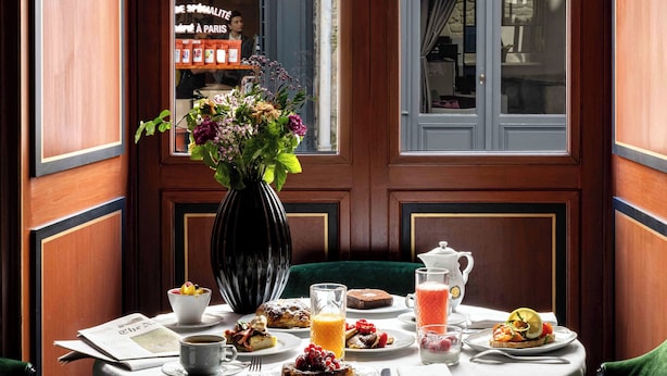 A breakfast table with a vase of flowers, plates of food, and a window view. - La Chambre du Marais (Paris)