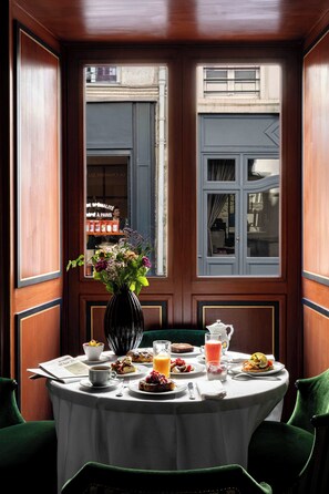 A breakfast table with a vase of flowers, plates of food, and a window view. - La Chambre du Marais (Paris)