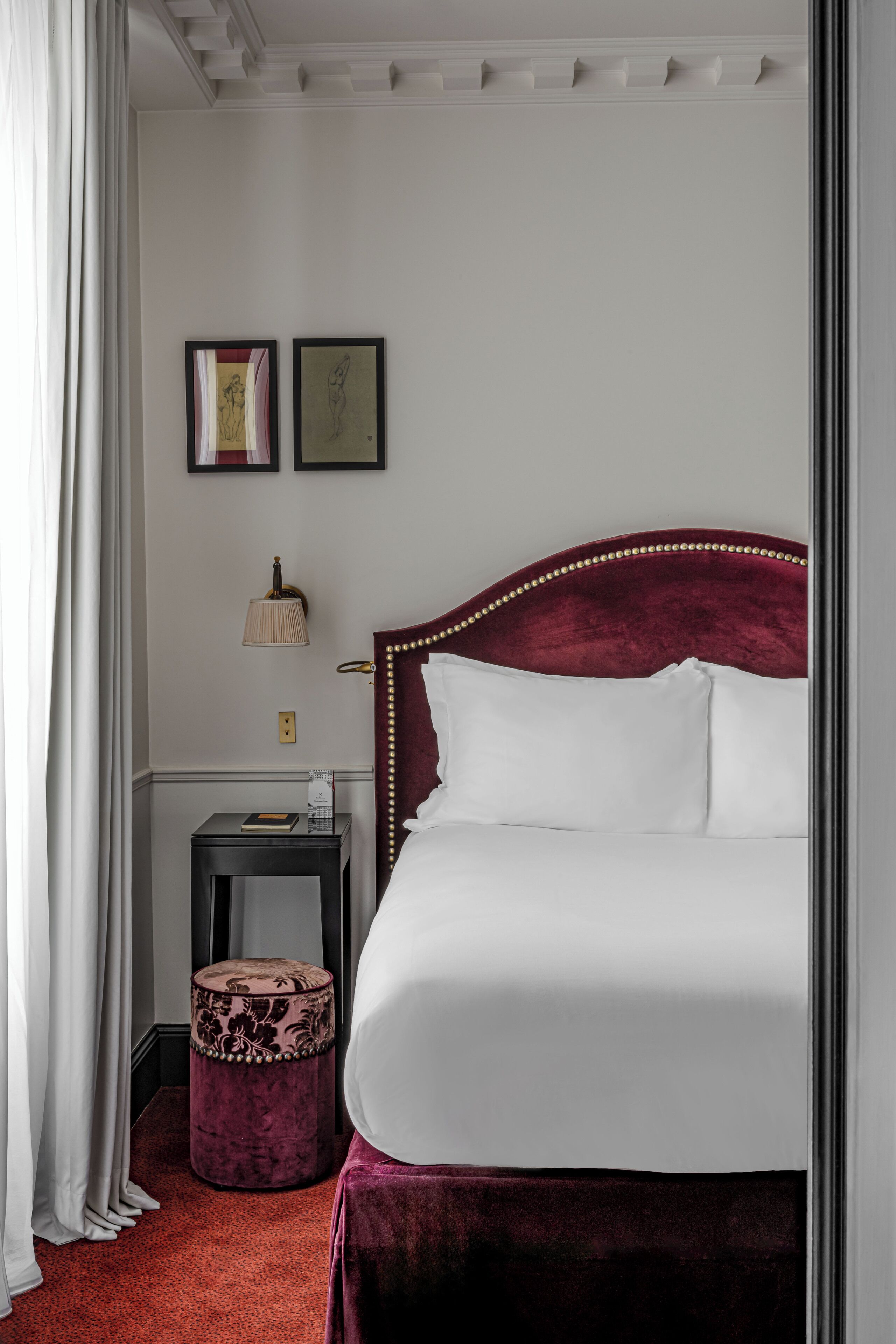 A neatly arranged hotel room with a large bed, a small side table, a lamp, and two framed pictures on the wall.