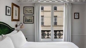 A hotel room with a bed, a window with curtains, and framed pictures on the wall. - La Chambre du Marais (Paris)