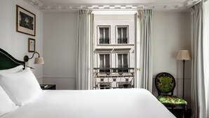 A hotel room with a large bed, a chair, a nightstand, and a view of a building through a window. - La Chambre du Marais (Paris)