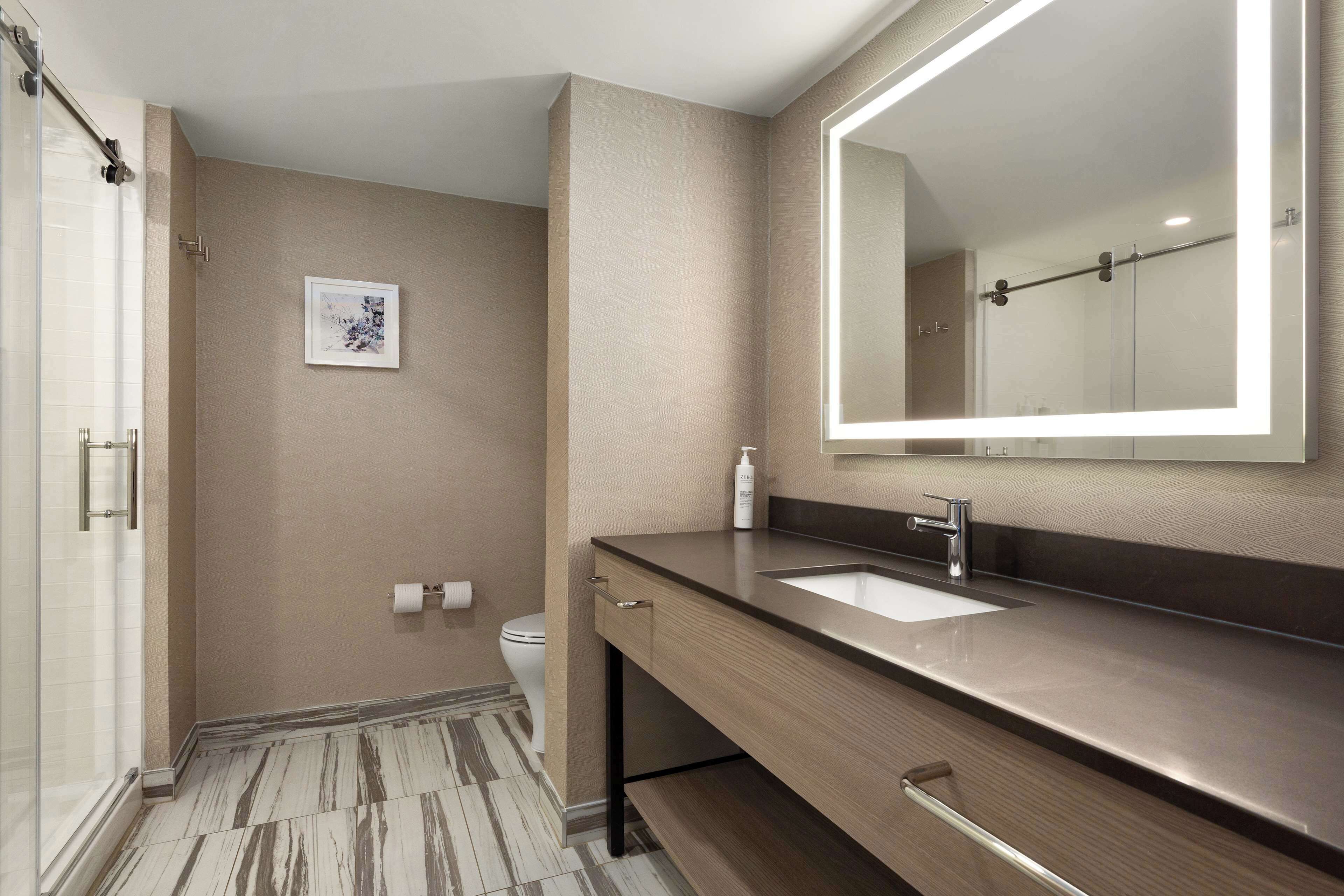 A modern bathroom with a large mirror, a sink, and a shower.