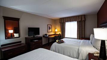 Habitación de hotel con dos camas, un escritorio, un televisor y una ventana con cortinas.